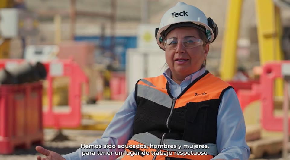 Worker in safety gear and helmet speaking at a construction site, Spanish text caption.